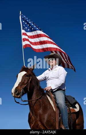 Un membro di un gruppo chiamato Cowboys per Trump, a cavallo, armato di una pistola e che porta una bandiera americana, partecipa a un rally pro-Trump. Foto Stock