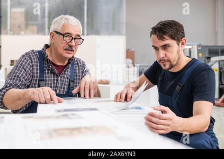 Lavoratori anziani e giovani concentrati seduti a una pila di pagine ed esaminando le carte stampate Foto Stock