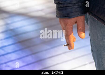 Colpo di closeup di una persona che tiene una smussatura mezzo-fumata sopra la strada Foto Stock