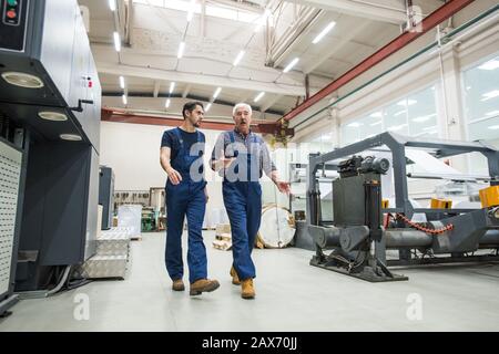 Esperto uomo anziano in mani gesturanti globali blu mentre interagendo con giovane lavoratore alla fabbrica di stampa Foto Stock