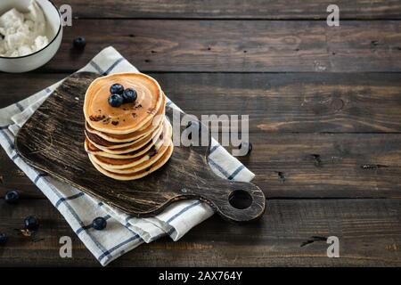 frittelle di ricotta con mirtilli su sfondo di legno scuro. Stile rustico. Cibo confortevole. Foto Stock