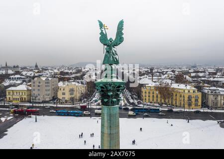 Budapest, Ungheria - veduta aerea della Piazza degli Eroi innevati con sculture d'angelo, autobus e via Andrassy in una mattinata invernale Foto Stock