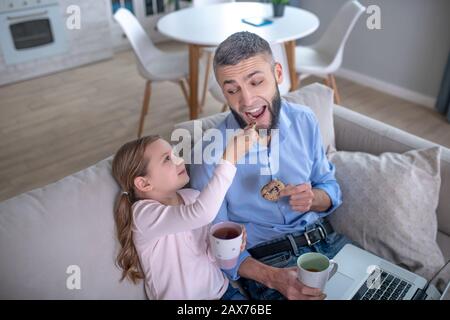 Piccola figlia premurosa che dà al papà un gustoso biscotto. Foto Stock