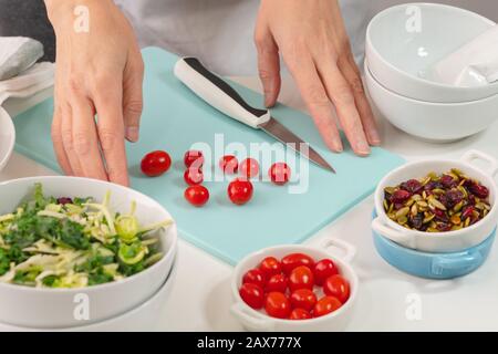 Donna che prepara insalata di verdure. Primo piano di verdure biologiche fresche, mix di cavolo, pomodori, mirtilli secchi e semi di zucca su un tavolo da cucina Foto Stock