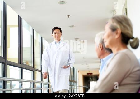 giovane medico asiatico che cammina nel corridoio dell'ospedale per incontrare i pazienti nell'area d'attesa Foto Stock