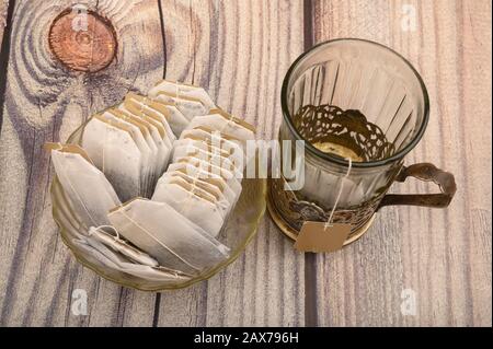 Bustine di tè in vaso di vetro e un bicchiere sfaccettato vuoto in una tazza d'epoca su sfondo di legno. Primo piano Foto Stock