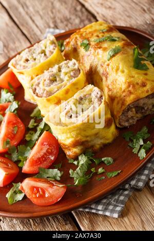 frittata rotolo farcito con carne, formaggio e sottaceti primo piano in un piatto sul tavolo. verticale Foto Stock