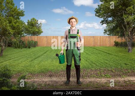 Giardiniere felice con una lattina d'acqua e un vaso di fiori in piedi in un cortile verde Foto Stock