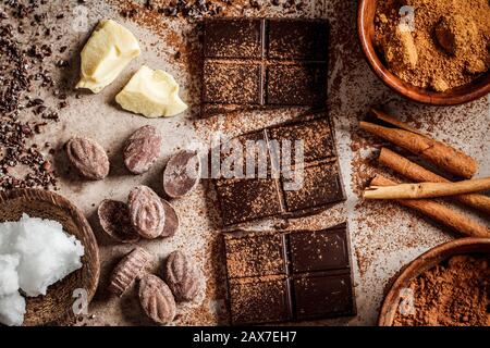 Ingredienti per la preparazione dello sfondo di cioccolato. Cacao, burro di cacao, zucchero, cannella e olio di cocco su sfondo scuro. Concetto di cioccolato. Foto Stock