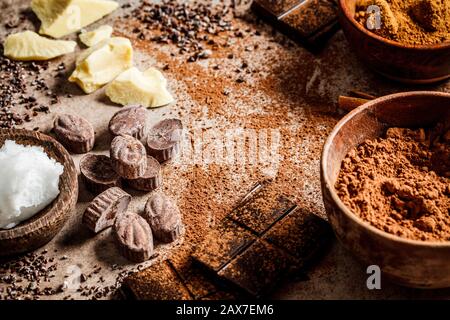 Ingredienti per la preparazione dello sfondo di cioccolato. Cacao, burro di cacao, zucchero, cannella e olio di cocco su sfondo scuro. Concetto di cioccolato. Foto Stock