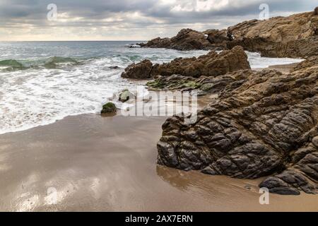 Spiaggia Di Leo Carrillo Vicino A Malibu, California. Sabbia e costa rocciosa. Onde, oceano verde, con nuvole in lontananza. Foto Stock