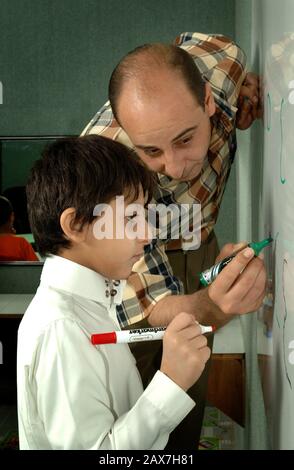 Insegnante arabo che insegna a un ragazzo come scrivere, Dammam Arabia Saudita. Foto Stock