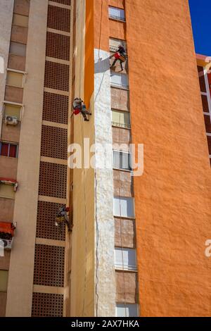 Accesso alla corda lavoratori pittura torre-blocco luminoso arancione, Villajoyosa, Costa Blanca, Spagna Foto Stock