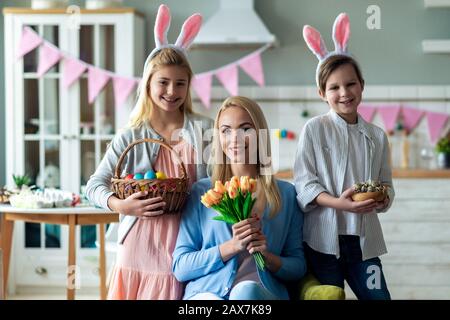 Ritratto di famiglia felice. Madre seduto e tenuto un mazzo di tulipani, figlio e figlia stanno tenendo un cesto con le uova di Pasqua. Foto Stock