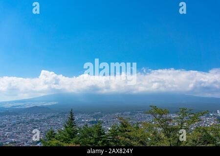 Veduta aerea della città di Fujiyoshida e del Monte Fuji che si rastrellano sulle nuvole nella giornata di sole. Prefettura di Yamanashi, Giappone Foto Stock