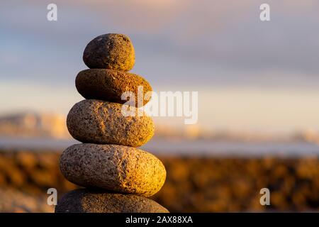 Pietra equilibrata pyramide sulla riva dell'oceano all'alba. Ciottoli di mare torre closeup simbolo stabilità, zen, armonia, equilibrio. Foto Stock