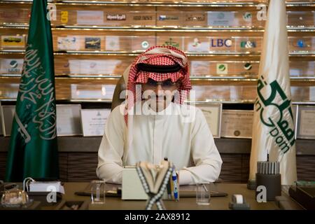 Ritratto di sua altezza reale Principe al Waleed Bin Talal al-Saud alla sua scrivania di fronte ad un muro pieno di loghi aziendali in cui ha partecipazioni al suo ufficio presso la holding del regno, Riyadh, Arabia Saudita. Foto Stock