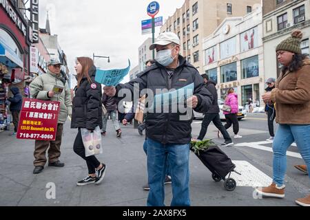 Un uomo americano cinese che indossa una maschera chirurgica porta fuori la lingua cinese che fa pubblicità a volantini su Main St. & Roosevelt Ave. A Chinatown, Flushing, NYC. Foto Stock