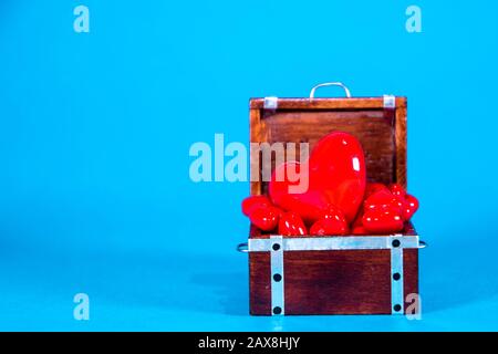 Una cassa del tesoro piena di cuori d'amore, presa su uno sfondo blu brillante. Foto Stock