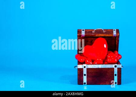 Una cassa del tesoro piena di cuori d'amore, presa su uno sfondo blu brillante. Foto Stock