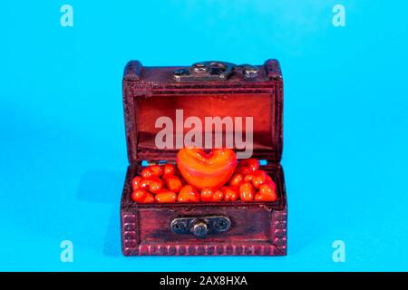 Una cassa del tesoro piena di cuori d'amore, presa su uno sfondo blu brillante. Foto Stock