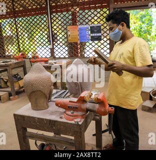 Un uomo che usa uno scalpello per scolpire teste di pietra a Artisans d'Angkor, un operaio co-operativo workshop, Siem Reap, Cambogia Foto Stock