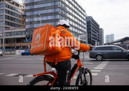 Un corriere di consegna del ciclo di Lieferando vestito in una uniforme arancione fluorescente brillante guida una bici per trasportare il cibo ad un cliente Foto Stock