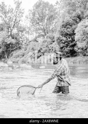 Barbuto brutale fisher la cattura di pesci trote con net. Se regolarmente del pesce si sa come gratificante e rilassante è la pesca. La pesca è un sorprendente accessibile ricreativo sport all'aperto. La pesca hobby. Foto Stock