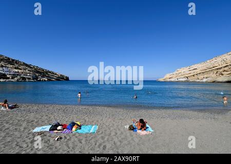 Matala, Grecia - 07 ottobre 2018: Persone non identificate sulla spiaggia di sabbia con le isole Paximadia sullo sfondo Foto Stock