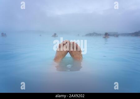 Piedi di una donna che bagna nella Laguna Blu vicino a Reykjavik con gente che bagna in questa sorgente calda naturale Foto Stock