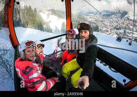 Cabina di guida per famiglie in funivia sulle piste da sci invernali. Famiglia in vacanza invernale sci viaggio prendere selfie all'interno di cabina con splendida vista sulle montagne Foto Stock
