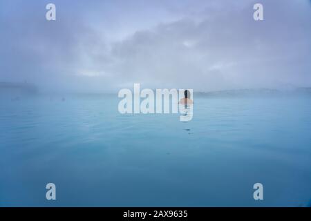 Donna che fa il bagno nella Laguna Blu vicino a Reykjavik con gente che fa il bagno in questa sorgente termale calda naturale Foto Stock