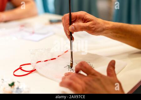 Primo piano di donna mani decorazione tessuto utilizzando vernice. Relax durante la pittura con pennello su tessuto Foto Stock