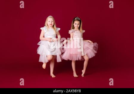 Belle ragazze principessa giocare in lusso rosa, bianco e argento abiti isolato su sfondo rosso. Viso divertente, emozioni diverse. Foto Stock