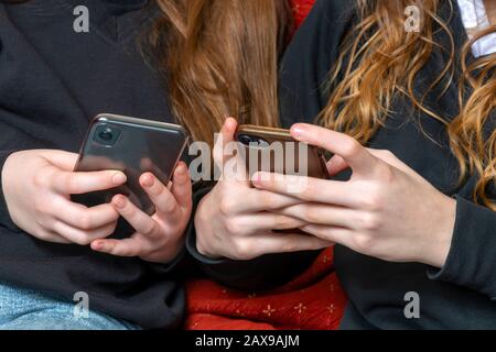 le ragazze teenage della scuola che sono cyber bullies o appena catching in su sui mezzi sociali entrambi sui telefoni là, spazio della copia del livello della mano sopra Foto Stock
