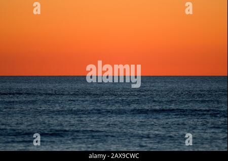 Un cielo senza nuvole all'alba si illumina di arancione su un oceano calmo e blu profondo. Foto Stock