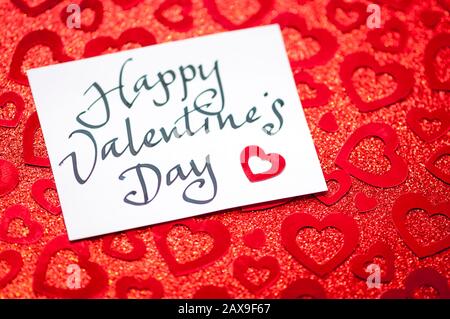 La nota del giorno Felice dei San Valentino scritta a mano si siede sullo sfondo sparkly coperto dai cuori casuali Foto Stock