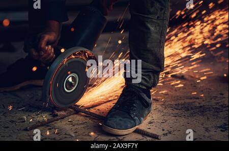 Saldatrice in azione, fotografia ravvicinata di scintille calde e luminose che volano da sotto la sega, macchina da taglio portatile in acciaio, duro lavoro, necessaria occupazione Foto Stock