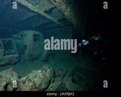 Un subacqueo illumina la forma spettrale di un camion militare della seconda guerra mondiale all'interno della stiva del relitto del Thistlegorm nel Rosso Sea.in Egitto durante la seconda guerra mondiale, quando è stata bombardata dalla forza aerea tedesca. Il Mar Rosso settentrionale è un cimitero letterale della gente di mare, le insidiose isole e barriere coralline che sorvegliano l'uscita dai golfi di Suez e Aqaba dopo aver reclamato numerose navi fin dai primi tempi. Oggi, i subacquei provenienti da tutto il mondo visitano i relitti del 19th secolo, sia le guerre mondiali, sia i tempi più recenti. Foto Stock