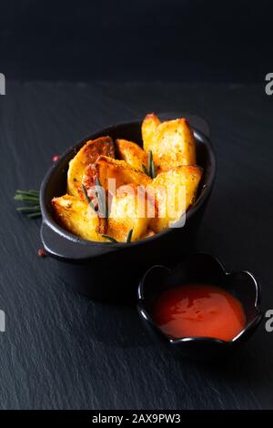 Concetto di cibo fatto in casa biologico Cotto Stagionato fette di patate In ciotola nera su piastra di pietra di ardesia nera con spazio copia Foto Stock