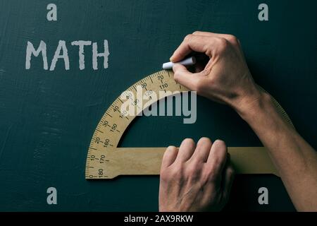 closeup di un uomo caucasico che usa un goniometro e il testo matematica, per la matematica, su una lavagna verde Foto Stock