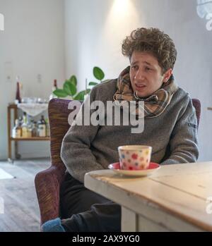 ritratto di giovane studente malato freddo esaurito è seduto al tavolo nel suo appartamento di fronte ad una tazza di tè Foto Stock