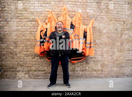 Berlino, Germania. 11th Feb, 2020. Ai Weiwei, artista cinese, è in piedi in studio di fronte alla sua opera 'sicurezza Giacche Zipped l'Altro Modo' nella 'parete della versione'. Le varie costruzioni di giacche di sicurezza, ganci e barre di ferro possono essere acquistate come parti individuali dallo sponsor Hornbach e assemblate da parti interessate stesse. Credit: Christoph Soeder/Dpa/Alamy Live News Foto Stock