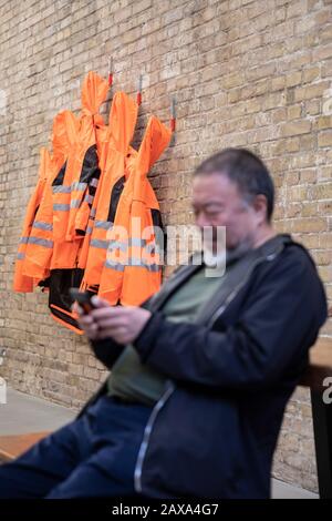 Berlino, Germania. 11th Feb, 2020. L'artista cinese ai Weiwei è seduto accanto al lavoro nella 'versione a parete' della sua opera 'Giacche di sicurezza Zipped l'Altro Modo' nel suo studio e guardando il suo smartphone. Le varie costruzioni di giacche di sicurezza, ganci e barre di ferro possono essere acquistate come parti individuali dallo sponsor Hornbach e assemblate da parti interessate stesse. Credit: Christoph Soeder/Dpa/Alamy Live News Foto Stock