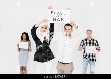 I giovani che mostrano slogan per la pace nel mondo, contro la guerra e il terrorismo. Persone multietniche, ragazza araba in hijab e caucasici, America Africana Foto Stock