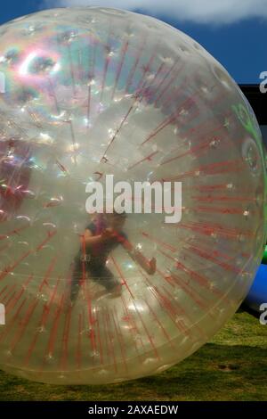 I bambini si divertono e si divertono a rotolare all'interno di una sfera Zorb o di una palla a bolle alla fiera Country Show Day presso la Silverdale School di Auckland Foto Stock