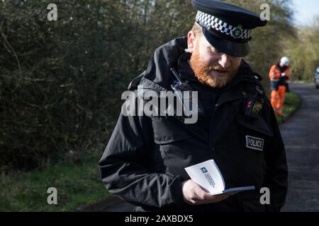 Denham, Regno Unito. 11 Febbraio 2020. Un ufficiale della polizia della Thames Valley legge da un libro intitolato ’Controterrorismo Policing’ mentre emette un avvertimento a un attivista ambientale di Extinction Rebellion che era stato ‘sa piedi bassi’ di fronte a un HGV che trasportava un veicolo elevatore JCB in un sito HS2. L'attivista è stato successivamente arrestato. Credit: Mark Kerrison/Alamy Live News Foto Stock