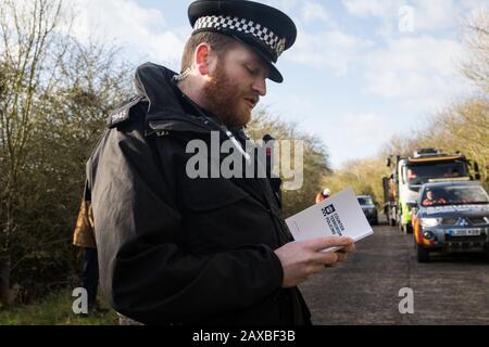 Denham, Regno Unito. 11 Febbraio 2020. Un ufficiale della polizia della Thames Valley legge da un libro intitolato ’Controterrorismo Policing’ mentre emette un avvertimento a un attivista ambientale di Extinction Rebellion che era stato ‘sa piedi bassi’ di fronte a un HGV che trasportava un veicolo elevatore JCB in un sito HS2. L'attivista è stato successivamente arrestato. Credit: Mark Kerrison/Alamy Live News Foto Stock