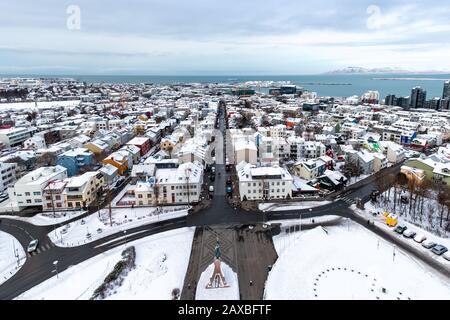 I tetti innevati di Reykjavik, capitale storica dell'Islanda. Case tradizionali, vista aerea, con la costa, il mare e i monti lontani Foto Stock