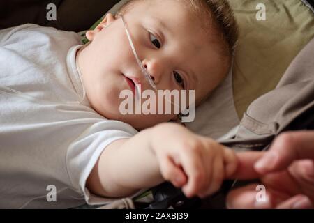 Bambino con paralisi cerebrale sta ottenendo ossigeno. Catetere nasale in un paziente pediatrico in ospedale. Supporto respiratorio. Bambino in terapia con ossigeno che tiene mo Foto Stock